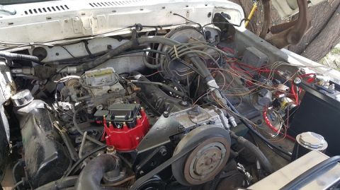 1978 Ford Bronco - The engine bay of a white 1978 Ford Bronco is shown with the hood open, revealing the engine, carburetor, distributor, and wiring. The vehi…