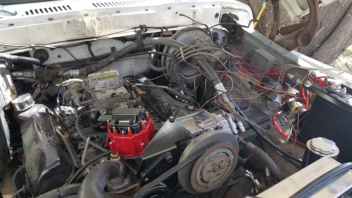 Engine bay of a white 1978 Ford Bronco, showing engine, carburetor, distributor, and wiring.