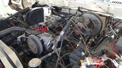 1978 Ford Bronco - The engine bay of a classic Ford Bronco, featuring a V8 engine with a carburetor, distributor, and various hoses and wiring. The view is fr…