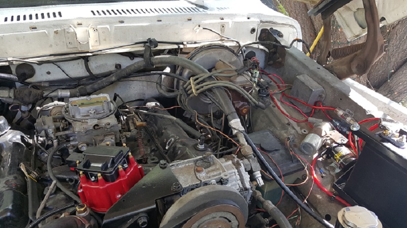 Close-up of a vintage Ford engine bay with carburetor, distributor, and wiring.