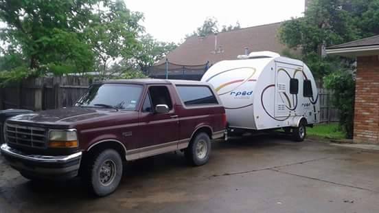 Maroon 1990s Ford Bronco towing a white teardrop trailer.