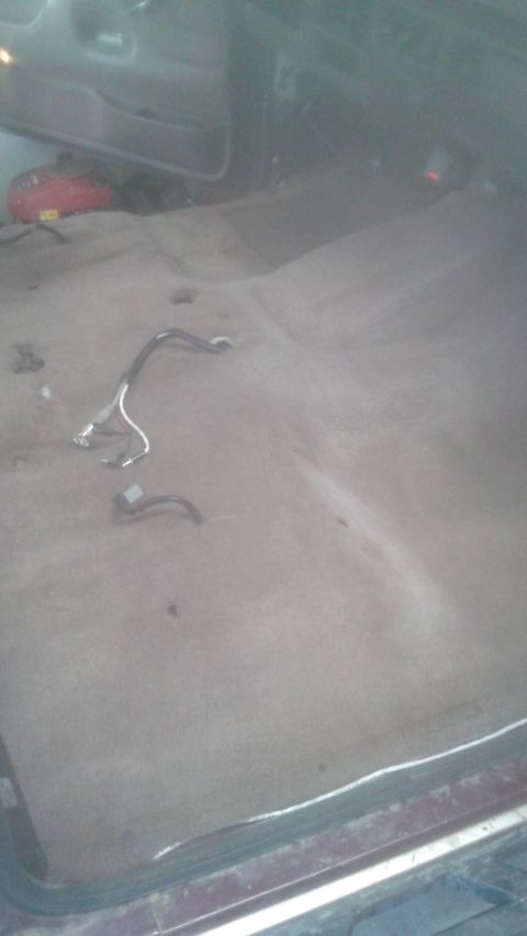 1996 Ford Bronco - The interior of a vehicle shows the carpeted floor with some wiring harnesses visible. A red object is partially visible in the background.