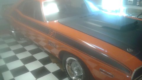 1996 Ford Bronco - A low-angle, slightly hazy view of the driver's side of an orange classic muscle car with black racing stripes and a black hood. The car ha…