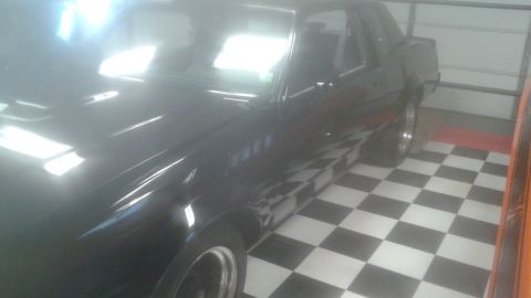 1996 Ford Bronco - A black coupe is parked in a garage with a black and white checkered floor. The car's hood and windshield are reflecting bright overhead li…