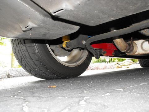 1994 Ford Bronco - The underside of a vehicle is shown, focusing on the rear tire, suspension components, and exhaust system. A bright red aftermarket part is…