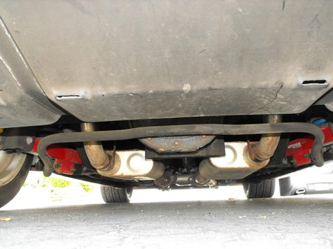 1994 Ford Bronco - Underside view of a vehicle, showing the exhaust system, differential, and a sway bar. Red components, possibly part of the suspension, are…