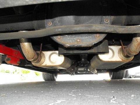 1994 Ford Bronco - The underside of a vehicle shows a dual exhaust system with mufflers and pipes leading to the rear. A red jack is visible on the left side…