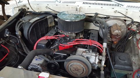 1978 Ford Bronco - The engine bay of a classic Ford truck is shown, featuring a V8 engine with red spark plug wires, a chrome air cleaner, and various hoses a…