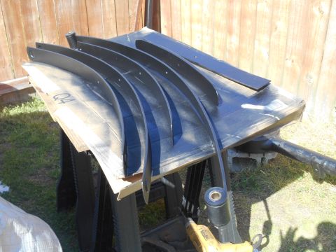 1972 Ford Bronco - Several black leaf springs are laid out on a workbench with a wooden fence in the background. A yellow power tool is visible in the foregro…