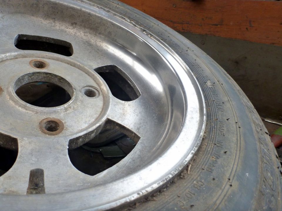 Close-up of a worn aftermarket wheel with a tire. Some text is visible on the tire sidewall