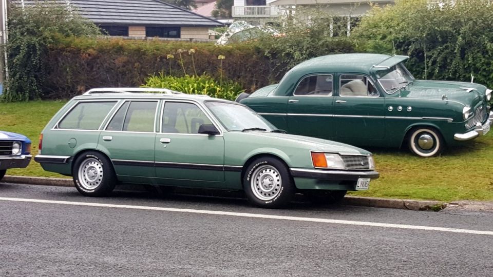 Green station wagon and a dark green sedan parked side-by-side on a street