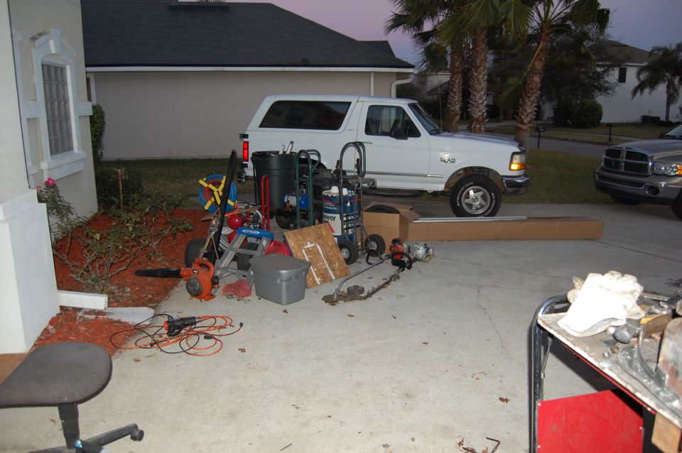White Ford Bronco parked in driveway with lawn equipment and a Dodge Ram truck.