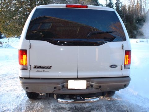 2003 Ford Excursion - The rear of a white Ford Excursion is shown in a snowy environment, reflecting a building in its windows.