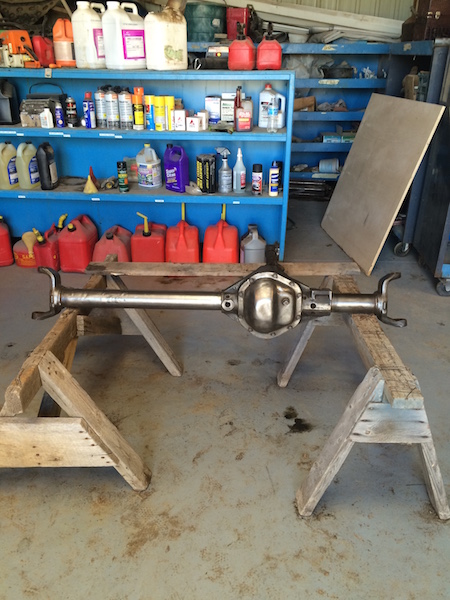 1981 Ford Bronco - A rear axle assembly is supported by two wooden sawhorses in a garage or workshop. Shelving units filled with various containers and suppli…