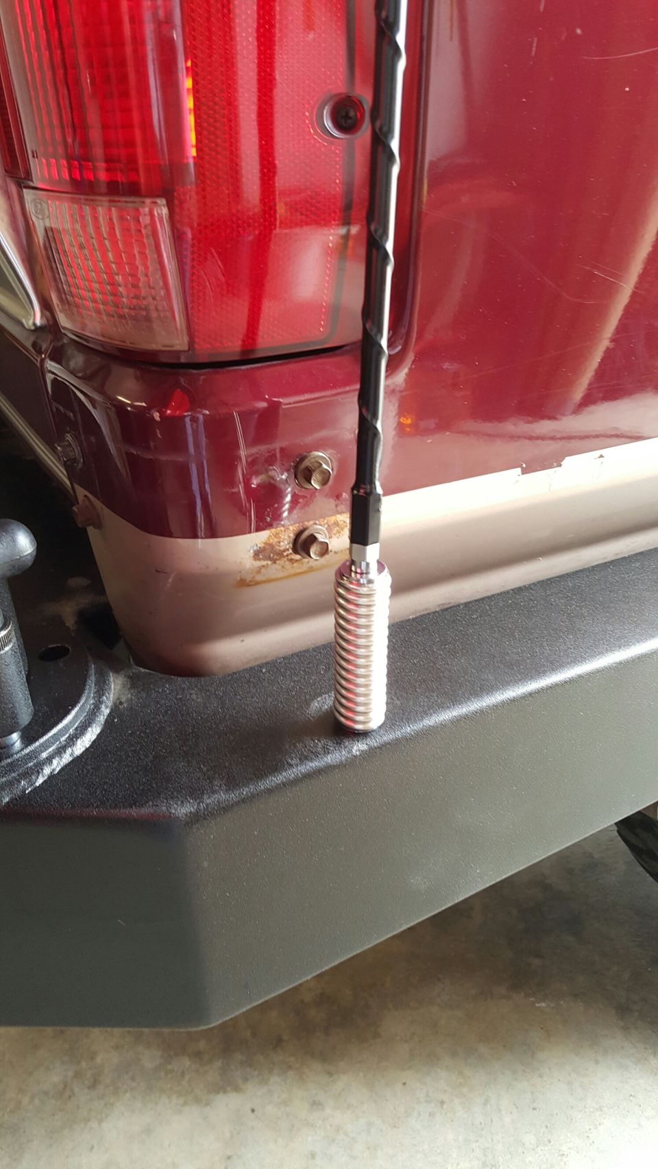 Whip antenna mounted on a textured rear bumper beside a red truck taillight