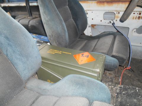1972 Ford Bronco - Interior view of a vehicle showing two blue fabric seats and a green ammunition box with hazard markings. The box has text that reads "Cart…