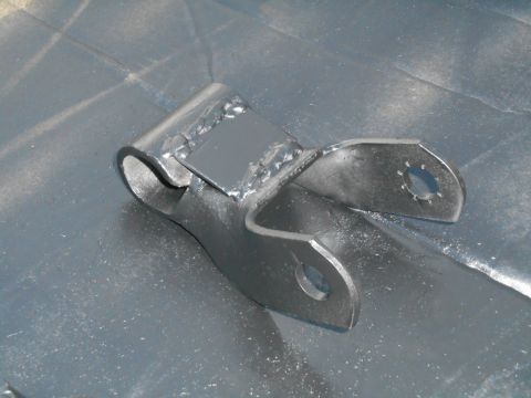 1972 Ford Bronco - A close-up, angled view of a metal suspension component, possibly a trailing arm or shackle, with two mounting holes and a welded reinforce…