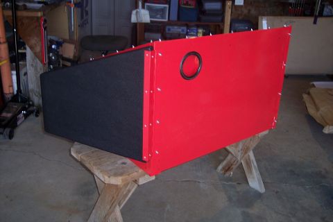 1990 Ford Bronco - A red and black custom-built enclosure is resting on a wooden sawhorse in a garage setting. The enclosure has a circular opening with a bla…