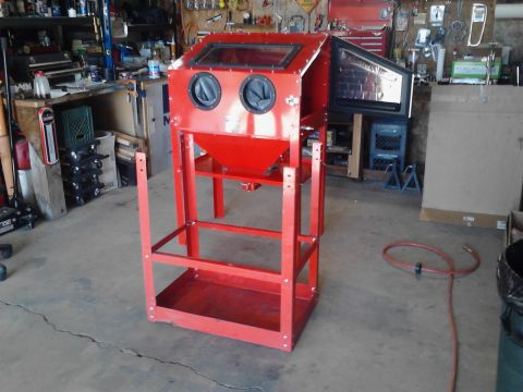 1990 Ford Bronco - A red sandblasting cabinet with two glove ports and a hinged door is set up in a cluttered garage or workshop. The cabinet is on a metal st…