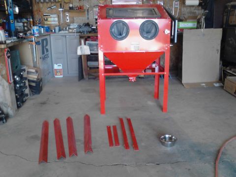 1990 Ford Bronco - A red sandblasting cabinet is the main focus of this garage scene. Various metal pieces and a small metal bowl are laid out on the concrete…