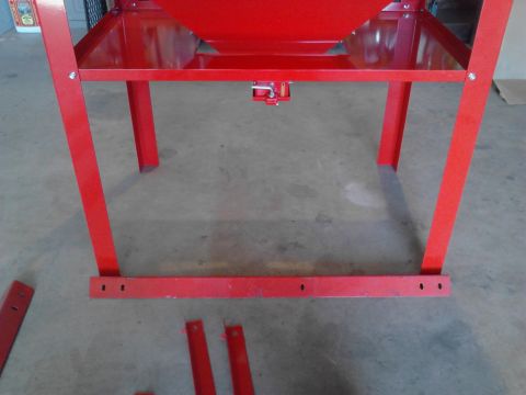 1990 Ford Bronco - A red metal frame with a hopper is shown from a low angle, sitting on a concrete floor. Several loose red metal pieces are scattered around…