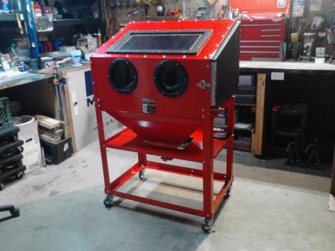 1990 Ford Bronco - A red sandblaster cabinet with two gloves and a viewing window sits on a rolling cart in a workshop. Tools and shelves are visible in the b…