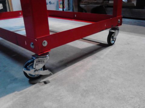1990 Ford Bronco - The red frame of a utility cart with four casters is shown on a concrete floor. One caster is locked with a brake.