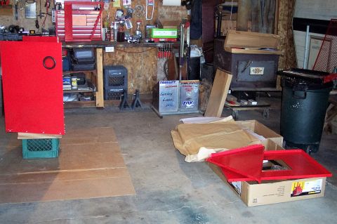 1990 Ford Bronco - A cluttered garage scene with various items including a large red cabinet, tool chests, storage bins, a trash can, and construction materia…