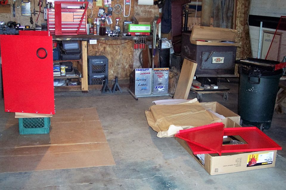 Garage scene with red cabinet, tool chests, trash can, and boxes.