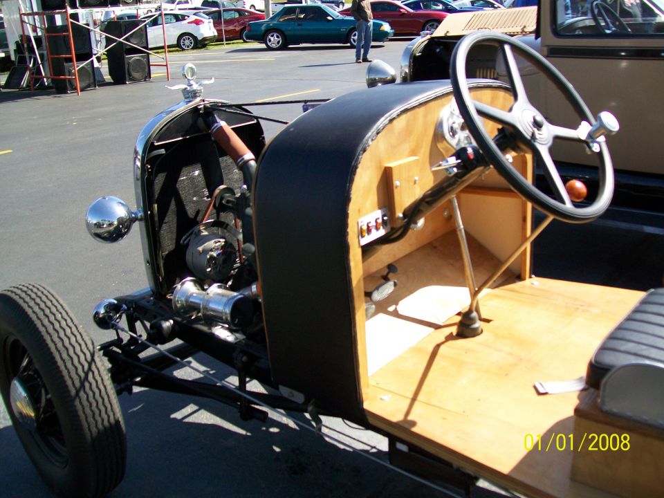 Interior of a hot rod showing steering wheel, wooden dash, and engine details.