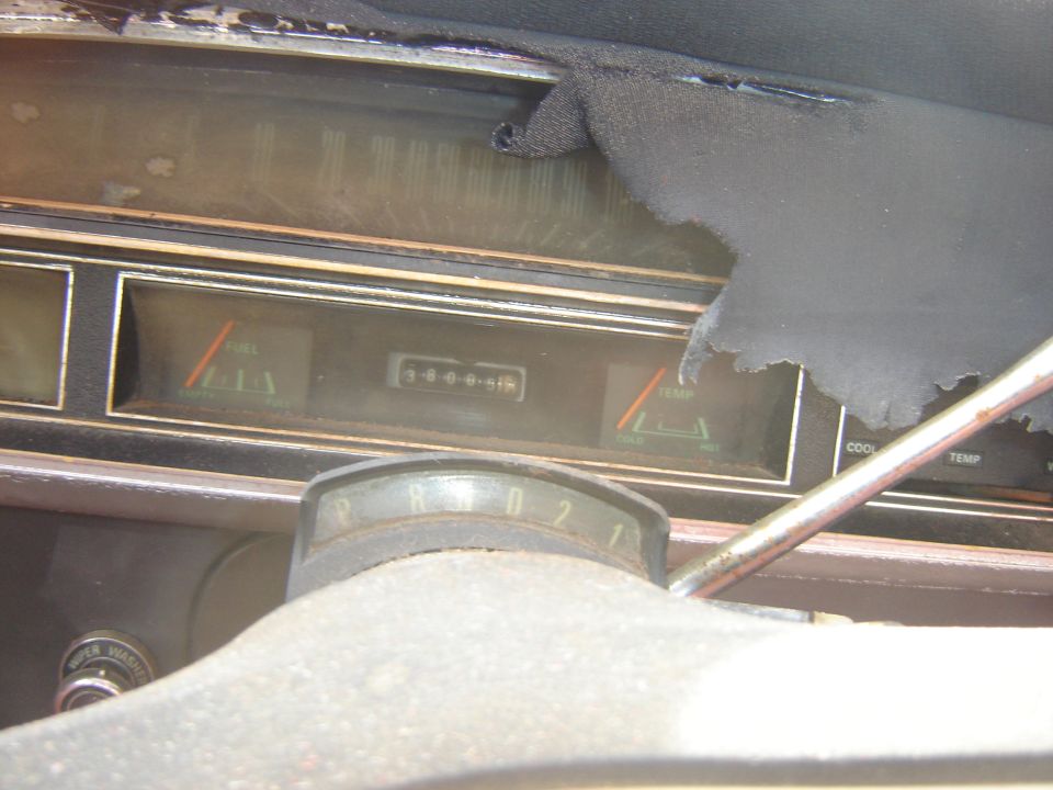 Vintage car dashboard with fuel, odometer, and temperature gauges. Torn fabric at the top.