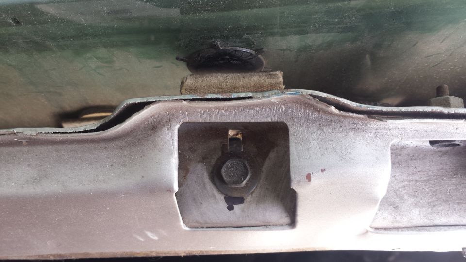 Underside of vehicle hood/trunk showing metal bracket with bolt and rubber bumper.