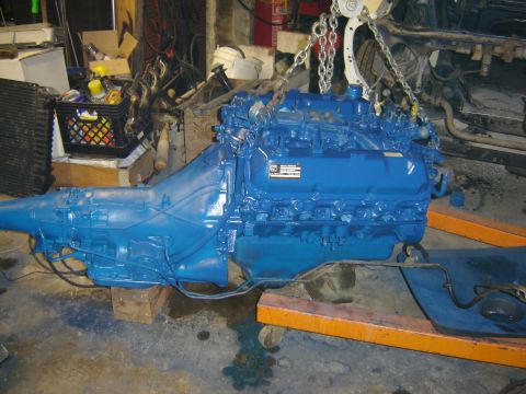 1971 Ford Ranchero - A bright blue painted engine and transmission assembly is suspended by chains from an engine hoist. The engine appears to be a V8 with a ch…
