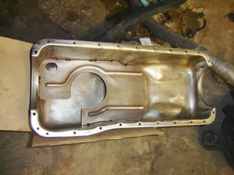 1971 Ford Ranchero - A clean, metallic oil pan sits on a piece of cardboard, likely part of a vehicle restoration or repair project. The oil pan has a series of…