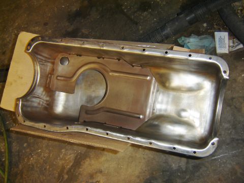 1971 Ford Ranchero - A clean, bare metal oil pan is laid out on a cardboard box. The oil pan has numerous bolt holes around its perimeter and a large circular o…