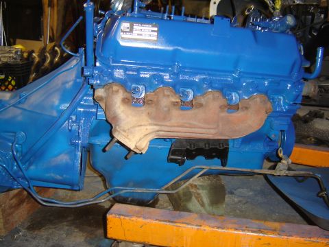 1971 Ford Ranchero - A blue painted V8 engine with a rusted exhaust manifold is mounted on an orange engine hoist. The engine bay and transmission housing are a…
