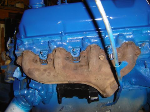 1971 Ford Ranchero - A close-up view of a blue painted engine with exhaust manifolds attached. The manifolds appear rusty and have some sort of mesh gasket mate…