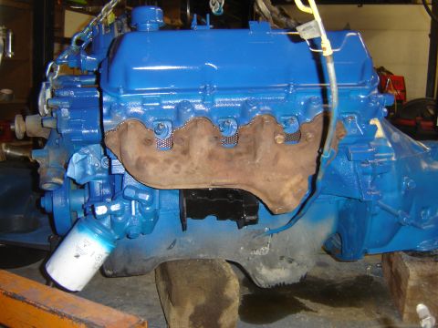 1971 Ford Ranchero - A blue painted Ford V8 engine with a rusty exhaust manifold is suspended by chains. A white oil filter with blue spray paint on it is attac…