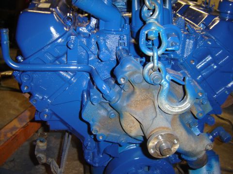 1971 Ford Ranchero - A close-up view of a bright blue painted engine block with a metal lifting hook attached to chains. The engine has some rusty components vi…