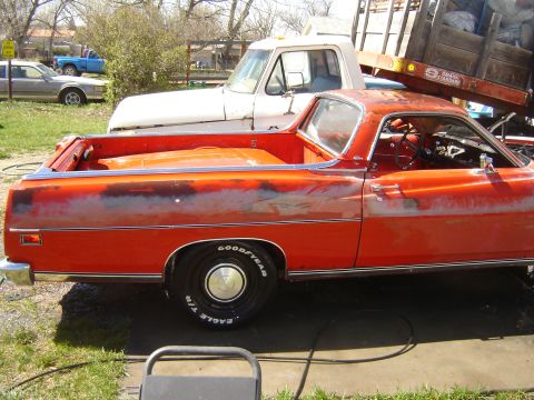 1971 Ford Ranchero - The side profile of a faded orange 1971 Ford Ranchero is visible, parked next to a white truck with a wooden trailer. The vehicle shows sig…
