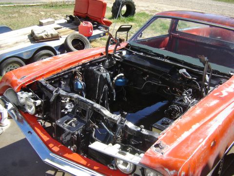 1971 Ford Ranchero - The front end of a classic orange Ford Ranchero is shown with its hood and engine removed, revealing the engine bay which appears to be coa…