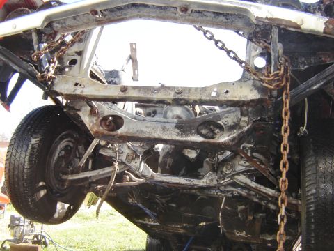 1971 Ford Ranchero - Underside view of a heavily rusted vehicle frame with chains attached. A tire and part of the suspension system are visible on the left.