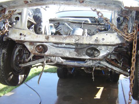 1971 Ford Ranchero - The heavily rusted and damaged front subframe and suspension components of a vehicle are visible, suspended by chains. The scene appears to…