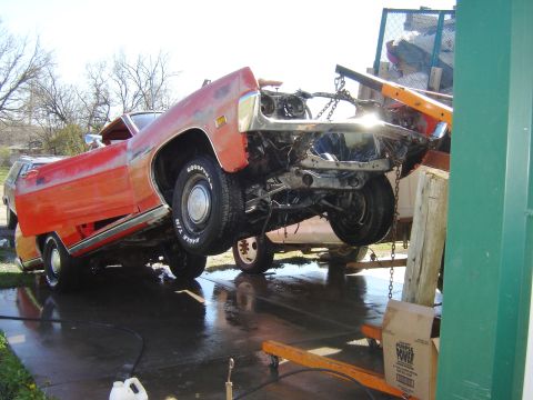 1971 Ford Ranchero - A bright orange 1971 Ford Ranchero is tilted upwards and suspended by chains and a hydraulic lift. The front of the vehicle is heavily dama…
