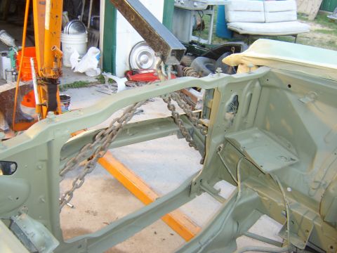 1971 Ford Ranchero - The front chassis of a classic vehicle, likely a 1971 Ford Ranchero, is shown painted in a matte olive green color. Chains are used to supp…