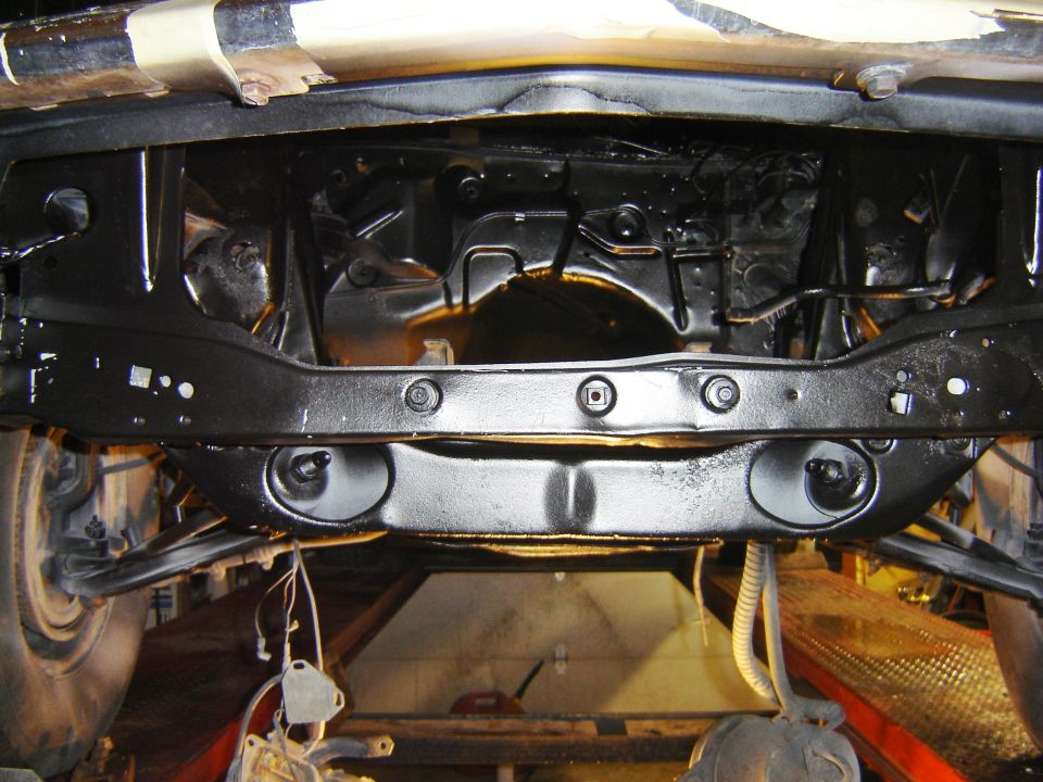 Underside of a black painted vehicle front suspension and subframe on a lift.