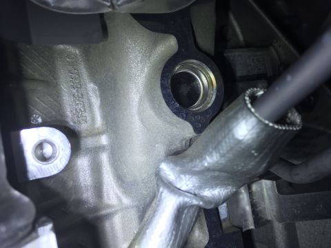 1994 Ford Bronco - A close-up view of a metal engine component with engraved text that reads "RFEJ7E-6030-EC". A black hose with a textured sleeve is visible…