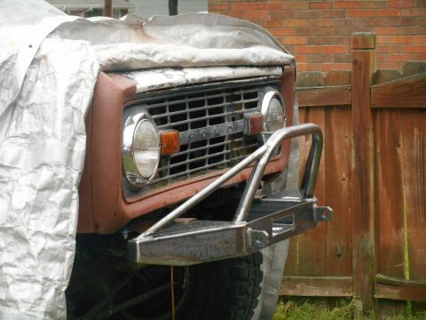 1972 Ford Bronco - The front of a classic Ford Bronco, partially covered by a silver tarp, is shown with a custom metal bumper. The vehicle is parked next to…
