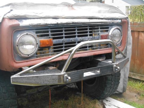 1972 Ford Bronco - Front view of a classic Ford Bronco with a custom metal bumper and brush guard. The vehicle is partially covered by a tarp and parked outdo…