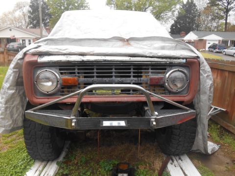 1972 Ford Bronco - The front of a classic Ford Bronco, partially covered by a tarp, features a custom metal bumper and grille. The vehicle is parked outdoors…